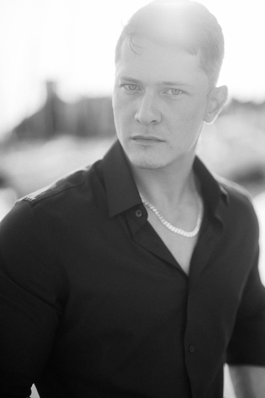 Black and white close-up portrait of a man in a dark shirt with soft backlight.