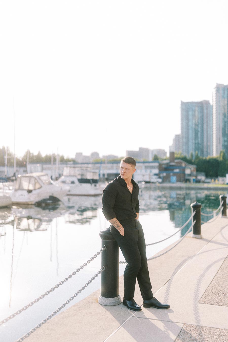 Man in black leans on a marina bollard beside boats and calm waterfront in Toronto.