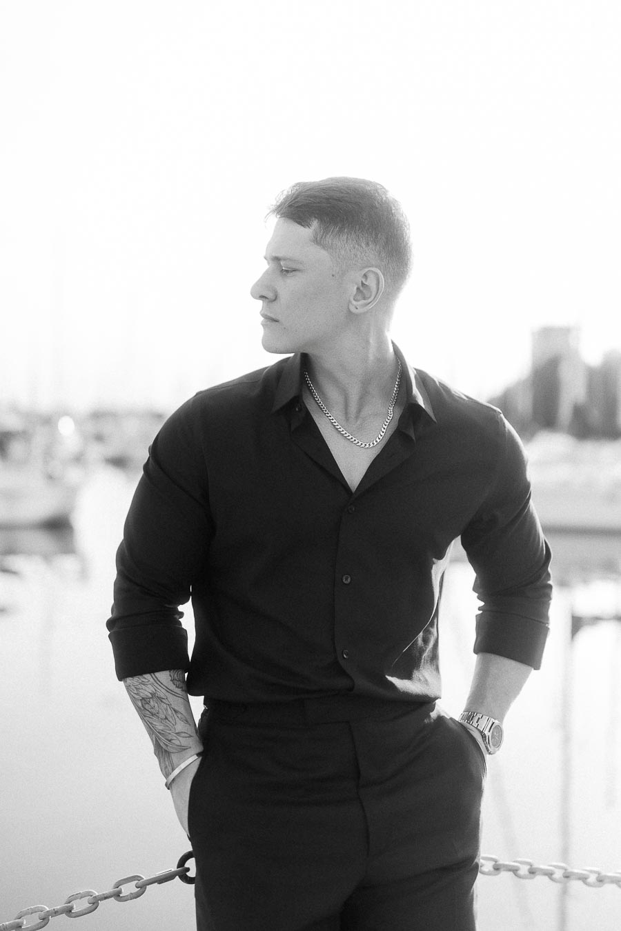 Black-and-white portrait of Alex in a dark shirt standing by a marina in Toronto