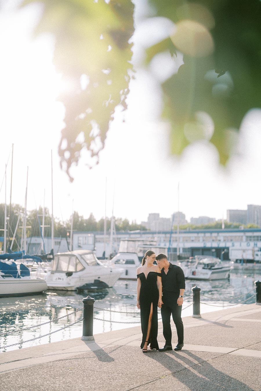 Couple in black outfits holding hands beside a Toronto marina with boats in soft evening light