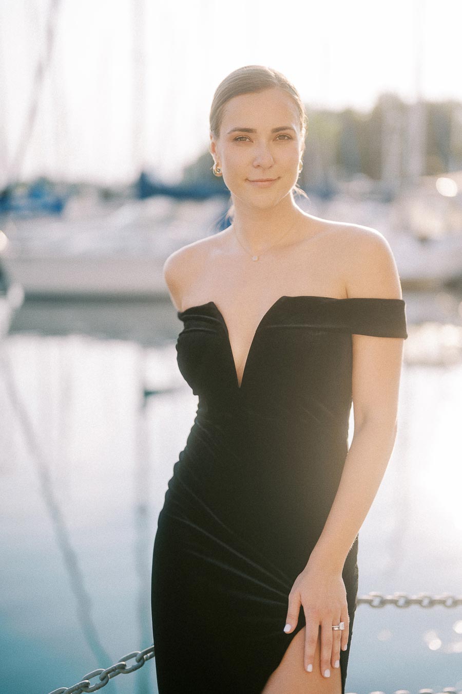 Bride-to-be in a black off-shoulder dress by a sunlit Toronto waterfront marina.