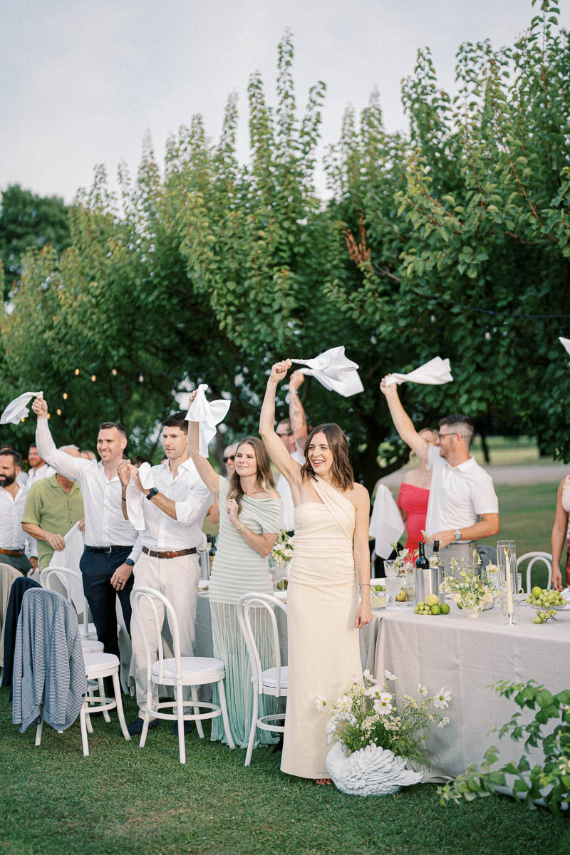 Guests cheer during the outdoor wedding dinner at Martin Estates in Niagara, captured in a candid moment.